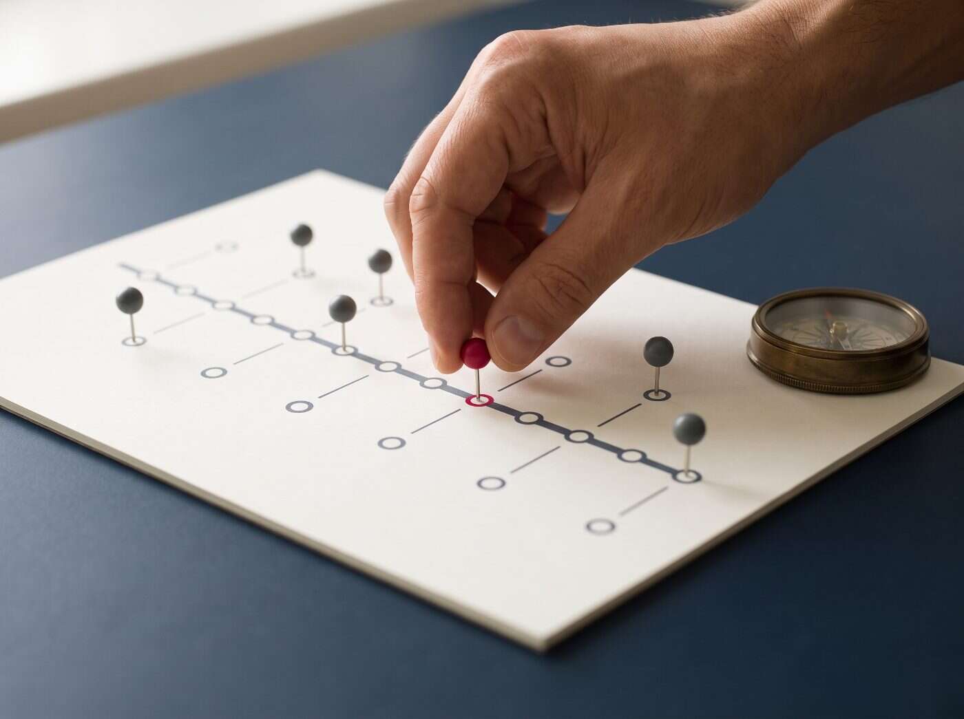 Hand placing a crimson pin on a printed twelve-step ISO 27001 roadmap laid on a navy desk