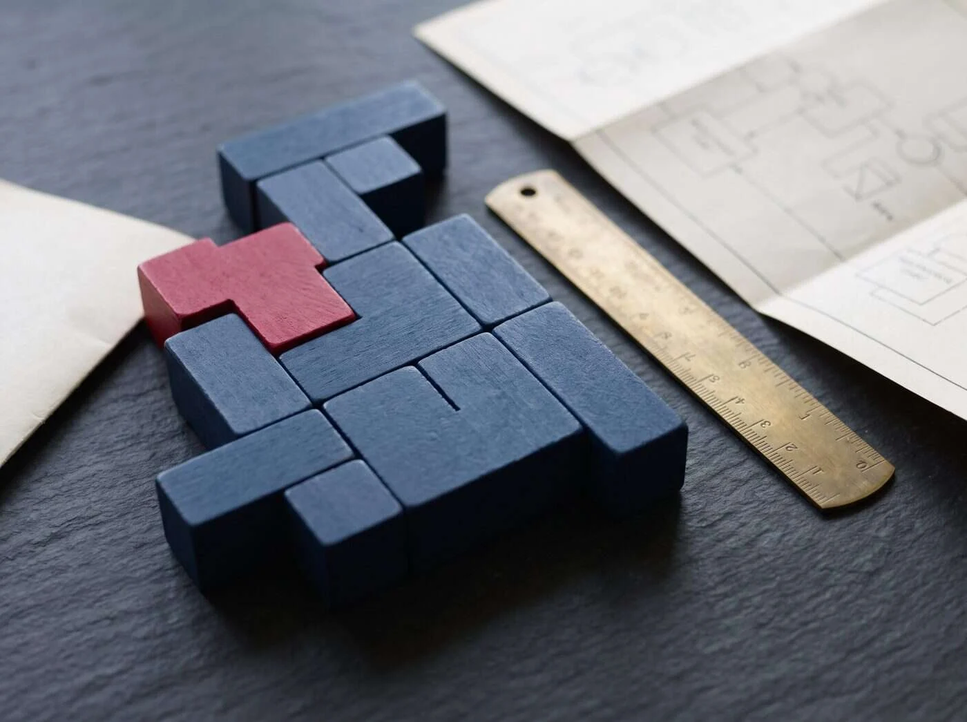 Interlocking navy wooden blocks with one crimson piece beside a brass ruler and a printed process chart, representing connected Odoo modules